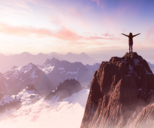 Image: A person standing with open arms on top of a mountain